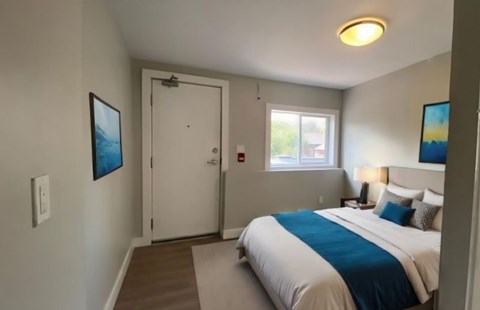 A bedroom with a bed, a window, and a painting on the wall.