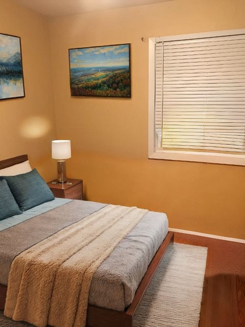 A bedroom with a bed, a lamp, and two paintings on the wall.