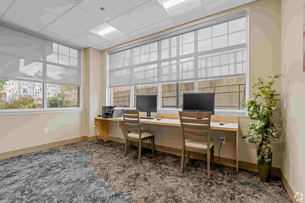 A room with a desk and chairs with a window in the background.