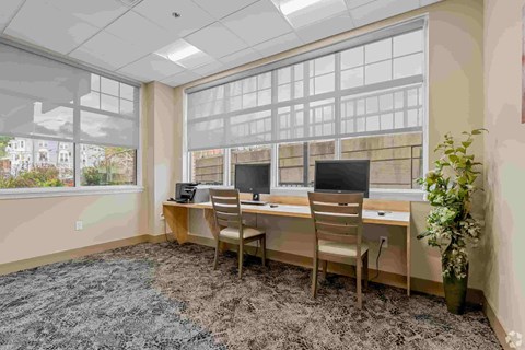 A room with a desk and chairs with a window in the background.