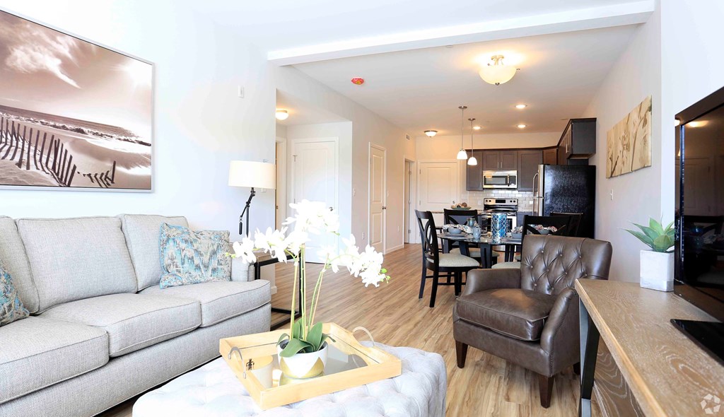 A living room with a grey couch, a coffee table with a tray, a vase with white flowers, and a painting on the wall.