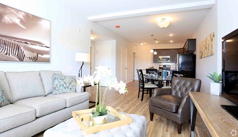 A living room with a grey couch, a coffee table with a tray, a vase with white flowers, and a painting on the wall.