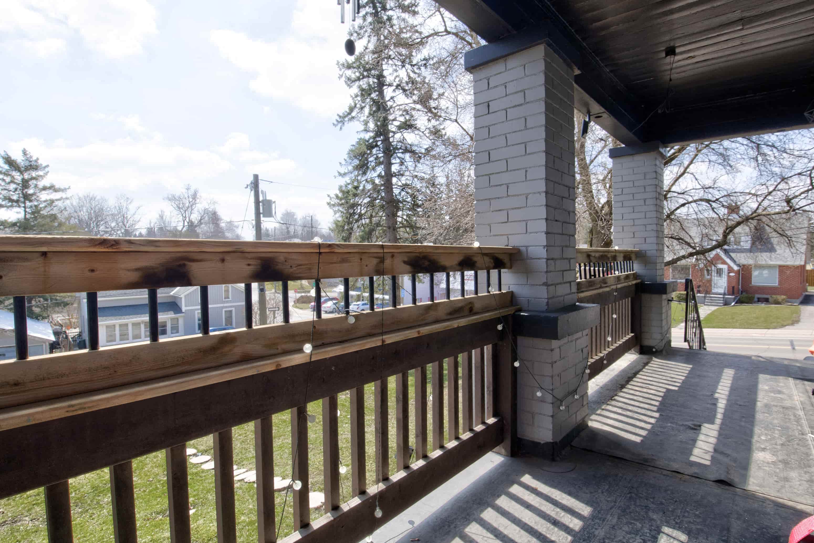 A wooden deck with a railing and a brick pillar.