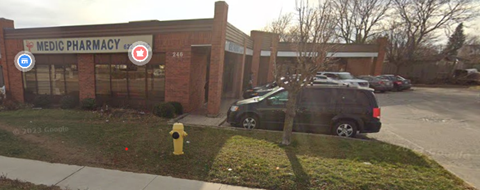 A black SUV is parked in front of a brick building with a sign that says "MEDIC PHARMACY.".