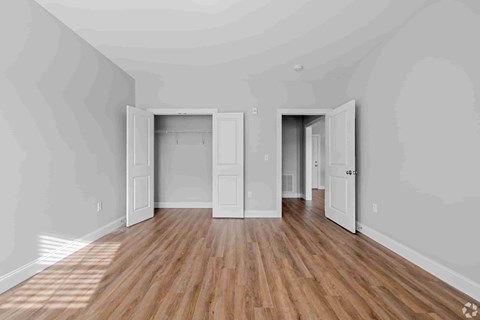 A room with wooden floors and white walls with two open doors.