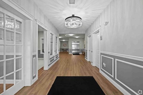 A long hallway with a black rug on the floor and a chandelier hanging from the ceiling.