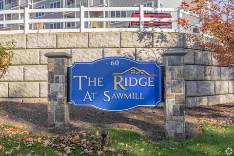 A blue sign that says "The Ridge at Sawmill" is mounted on a stone wall.