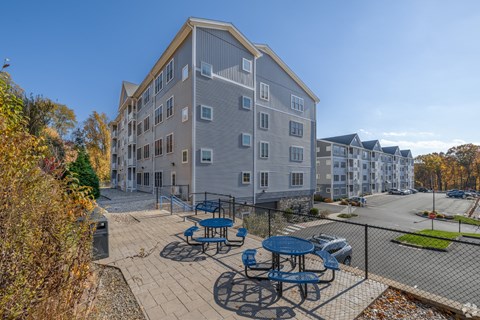 A grey apartment building with a patio and picnic tables.