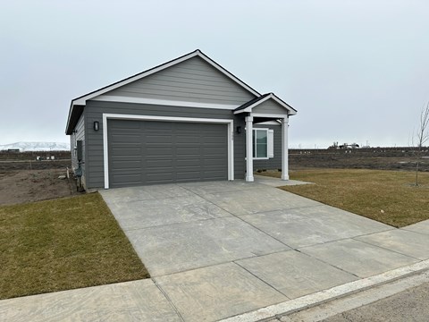 A two-car garage with a grey roof and a white door is situated in a grassy area.