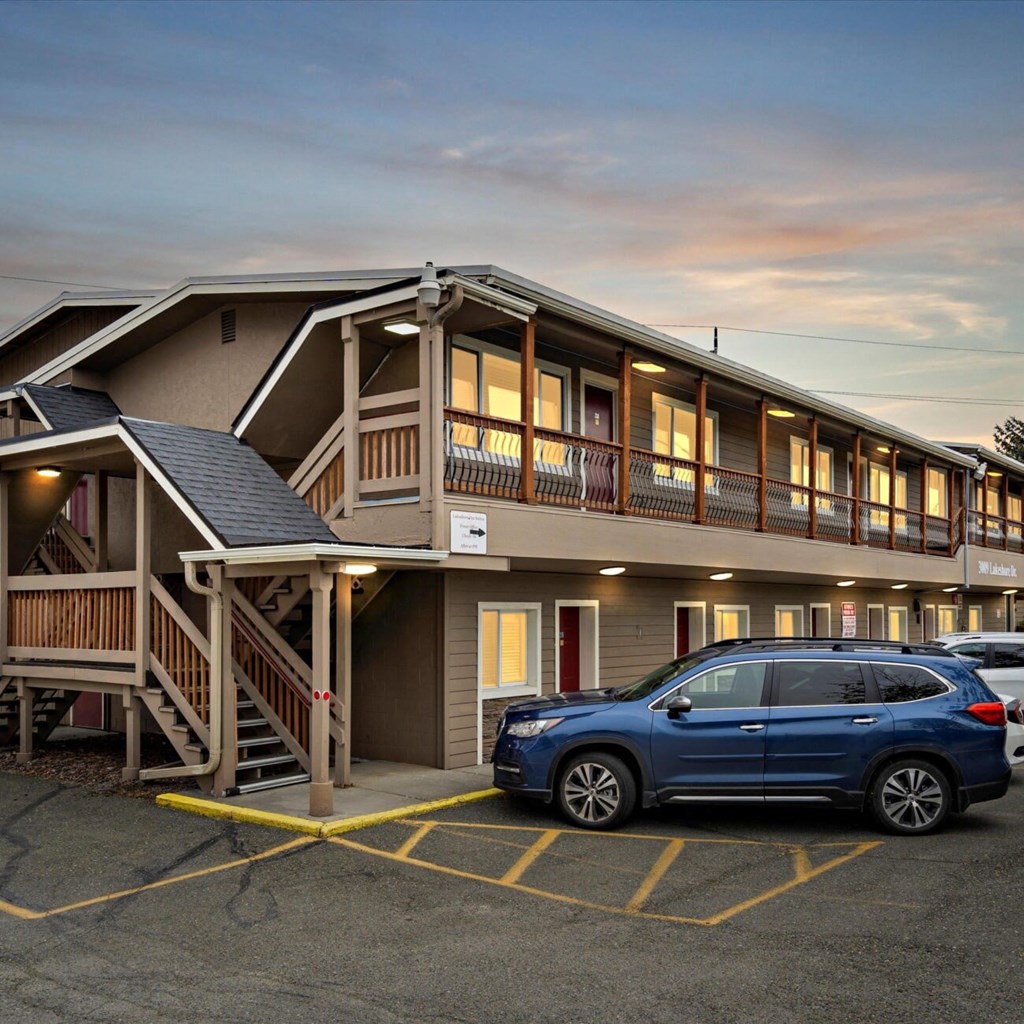 A blue SUV is parked in a parking lot in front of a building with a wooden deck.