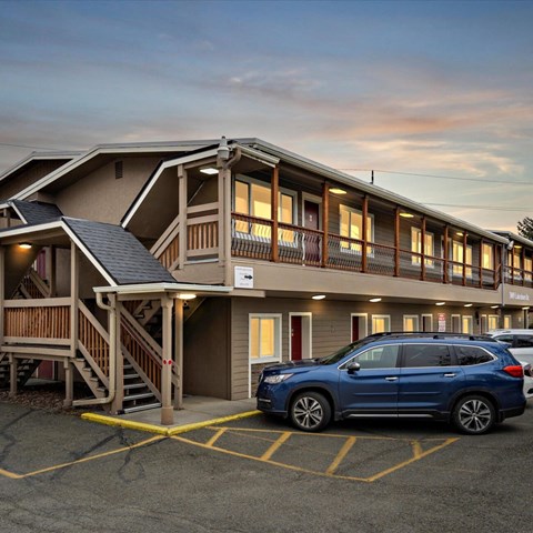 A blue SUV is parked in a parking lot in front of a building with a wooden deck.