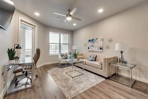 A living room with a white couch, a glass coffee table, and a ceiling fan.