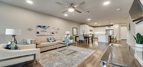 A modern living room with a white sofa, a glass coffee table, and a ceiling fan.