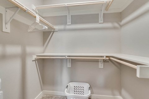 A white laundry basket sits on the floor of a white pantry.