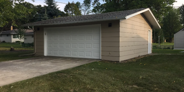 A tan garage with a white door is situated in a grassy area.