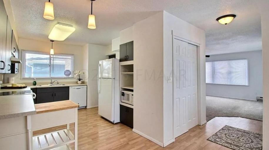 A kitchen with white appliances and a white door leading to a hallway.