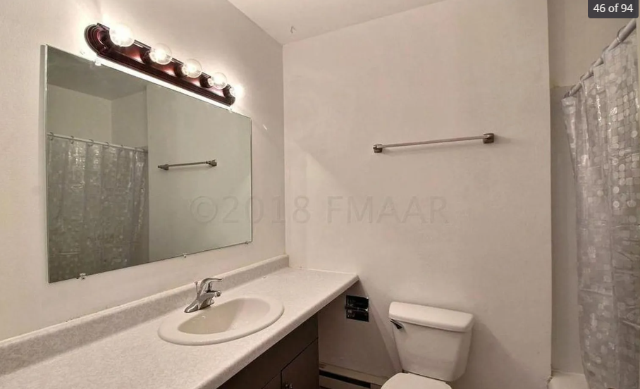 A white bathroom with a sink, toilet, mirror, and shower curtain.