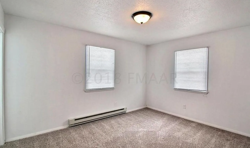 A room with a carpeted floor, a window with blinds, and a ceiling light.