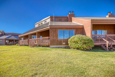 A house with a brown wooden exterior and a green lawn in front.
