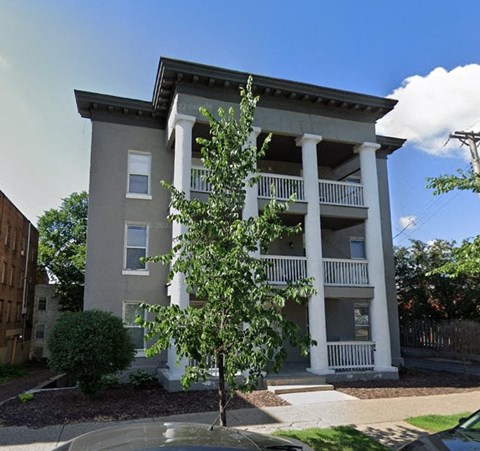 A tree stands in front of a two-story building with white columns.