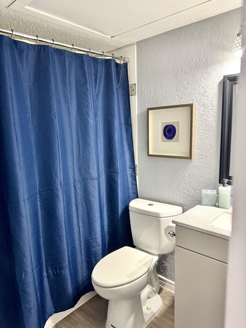 A white toilet in a bathroom with a blue shower curtain.