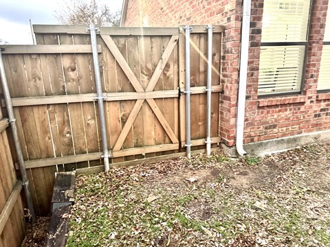 A wooden fence with metal posts is in front of a brick building.