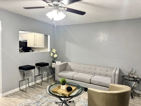 A living room with a grey couch, a glass coffee table, and a ceiling fan.