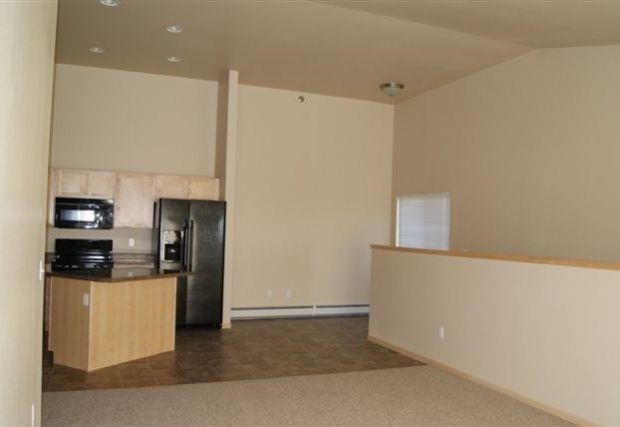 an empty living room with a refrigerator and a kitchen