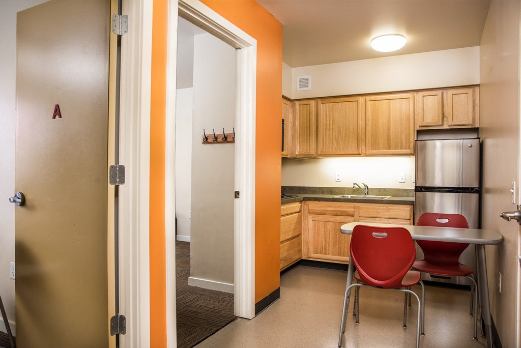 A kitchen with a red chair and a fridge.