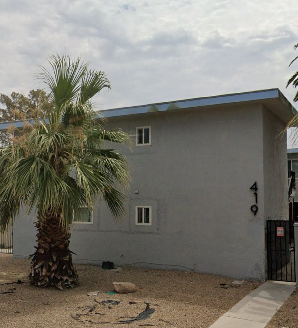 A grey house with a blue roof and a palm tree in front.