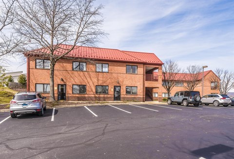 A parking lot in front of a red building with cars parked.