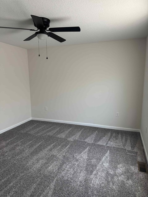 A room with a ceiling fan and carpeted floor.