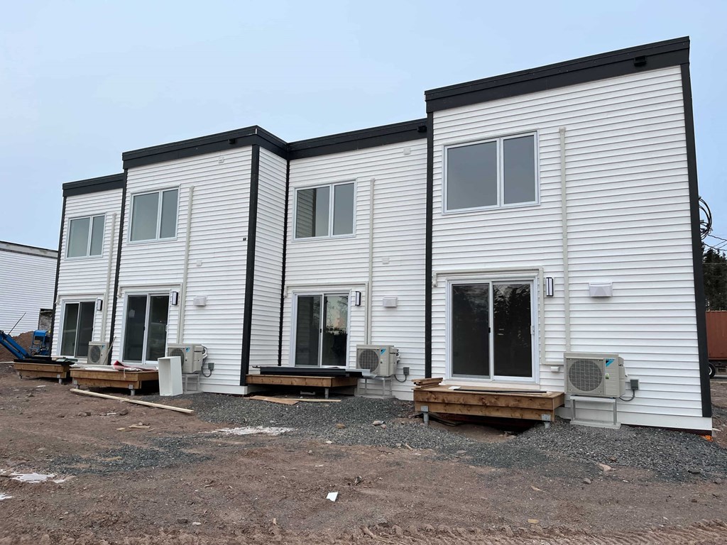 Three white houses with black trim are built on a gravel lot.
