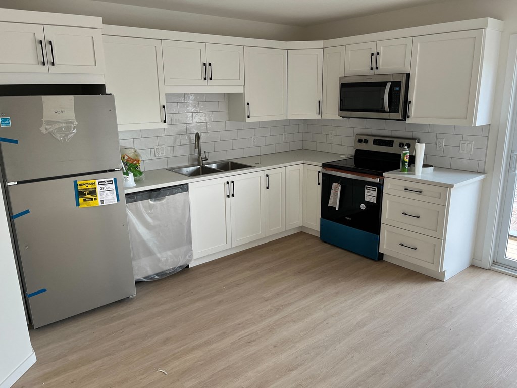 A kitchen with a refrigerator, microwave, oven, and sink.