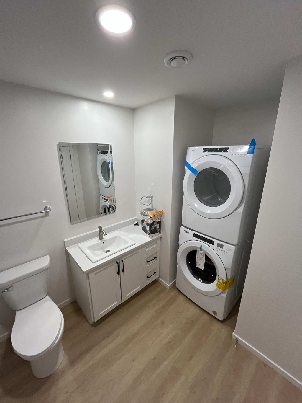 A small bathroom with a toilet, sink, mirror, and a washing machine.