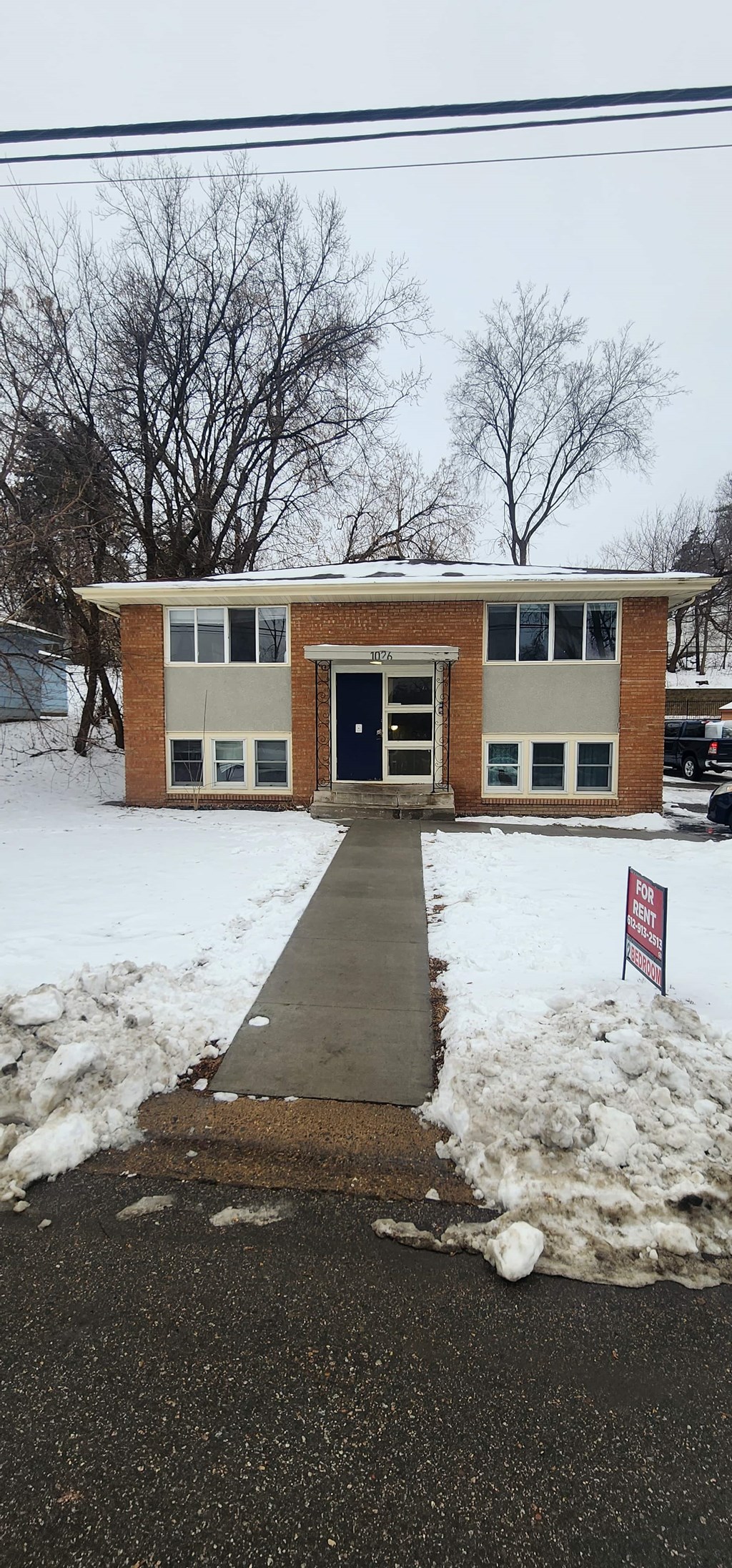 A small building with a black door is surrounded by snow.