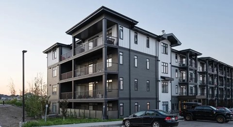 A black car is parked in front of a modern apartment building.