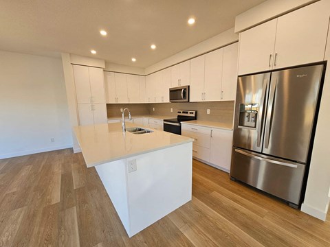 A modern kitchen with a stainless steel refrigerator and wooden flooring.