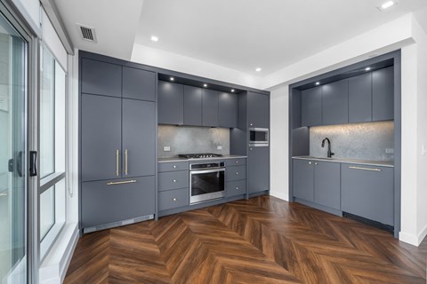 A modern kitchen with dark grey cabinets and wooden flooring.