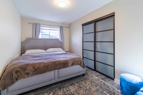 A bedroom with a bed, a window with curtains, and a blue chair.