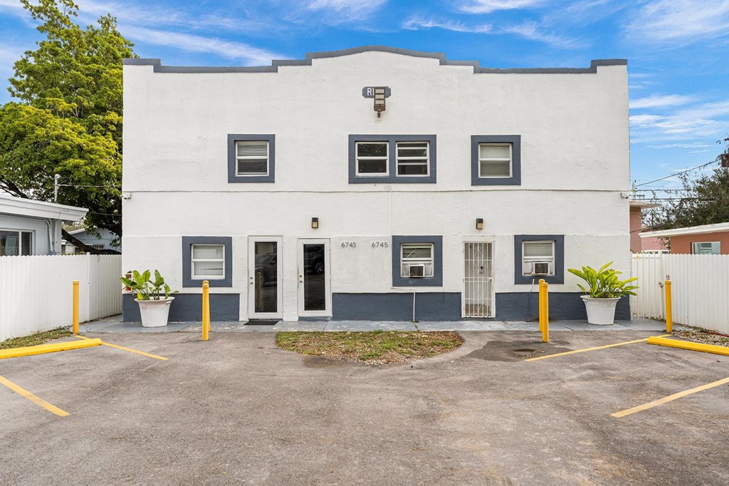 A white building with a black door and windows with yellow lines in front.