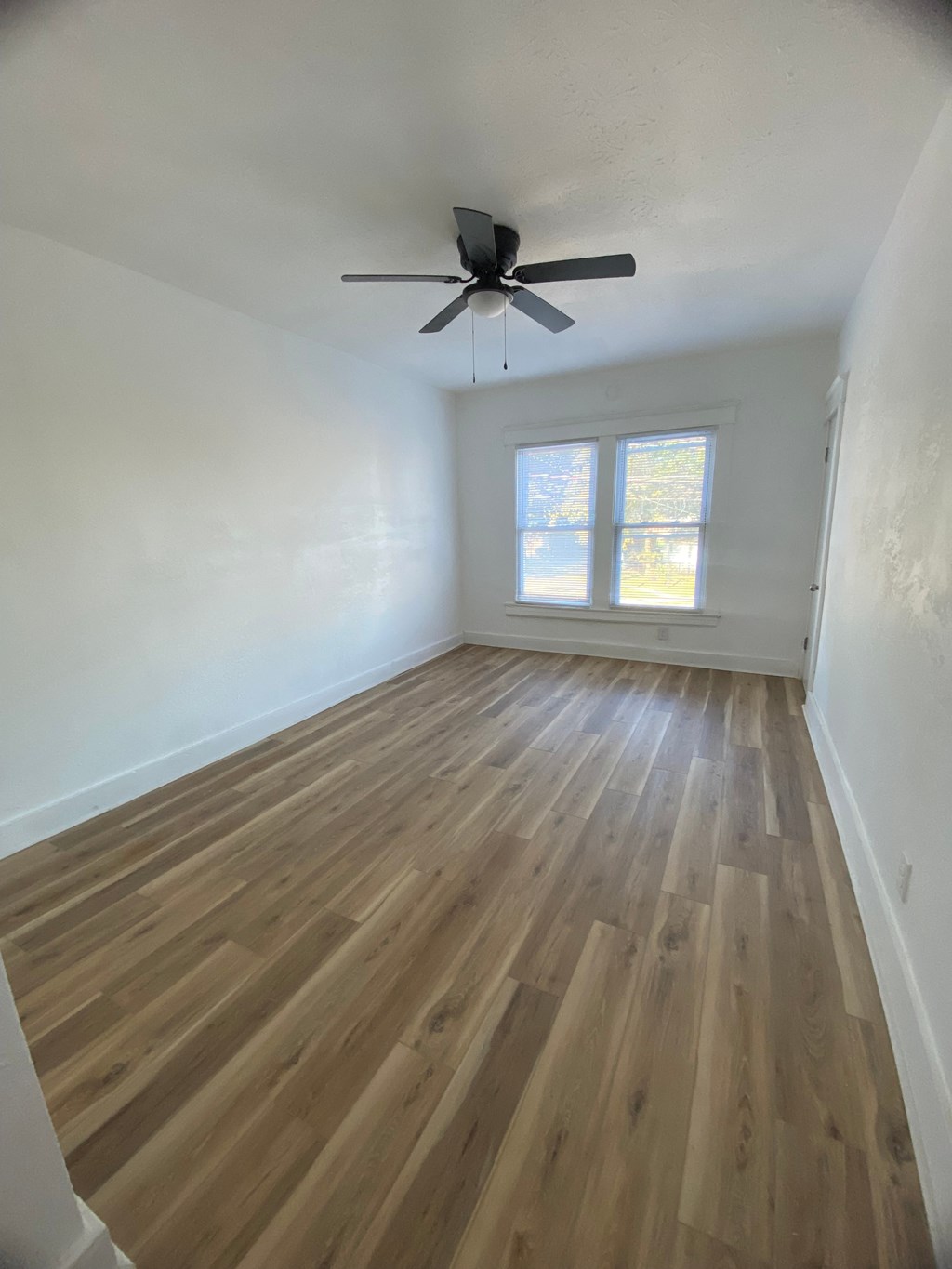 A room with a ceiling fan and wooden flooring.