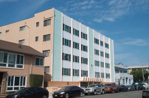 A large building with a white and blue facade is surrounded by parked cars.