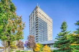 A tall building stands in front of a clear blue sky with trees in the foreground.