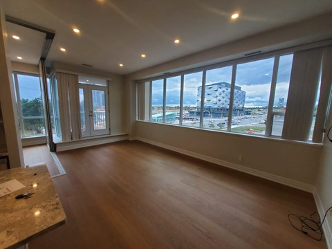 A room with wooden floors and a marble table with a view of a pool and buildings outside the window.