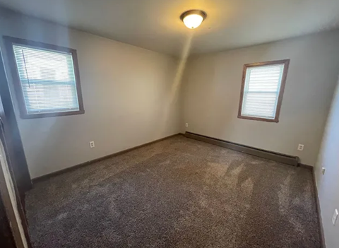 A room with a carpeted floor and two windows.