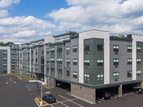 A parking lot in front of a grey building with cars parked.