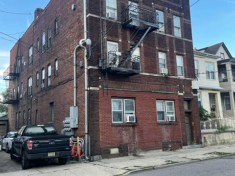 A black truck is parked on the sidewalk in front of a red brick building.