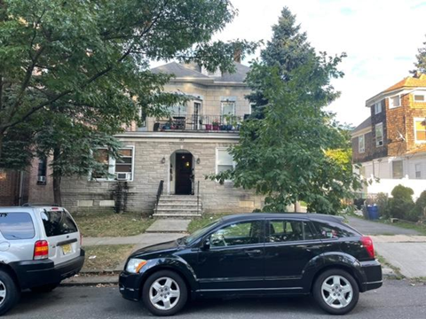 A black car is parked on the street in front of a house.