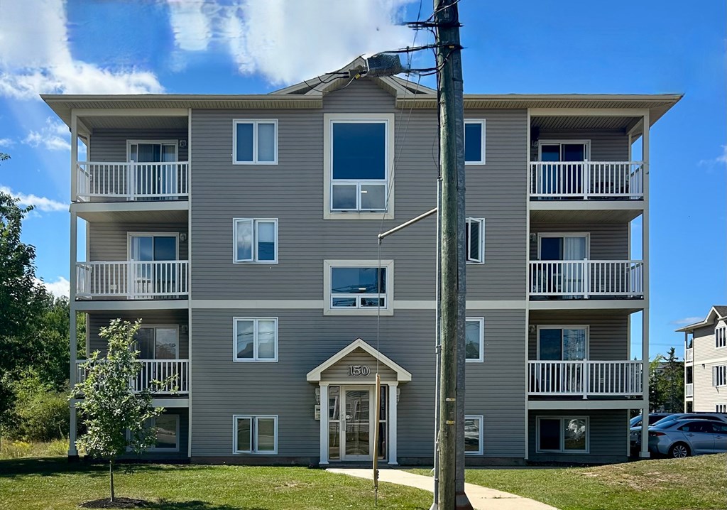 A grey apartment building with a tree in front of it.